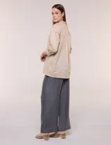 Camisa de silueta holgada y largo extendido, confeccionada en poplín elástico de color blanco. Presenta cuello solapa abierto en V con cartera frontal de abotonadura oculta, hombros caídos y mangas tres cuartos. Cuenta con espalda con canesú, pliegue central y ruedo recto con pequeñas aberturas laterales.