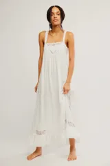 Vestido largo slip blanco de tela liviana y semitransparente, con silueta trapecio, escote cuadrado, tiras regulables, detalles de encaje, volado en el ruedo y espalda descubierta con lazo de ajuste.