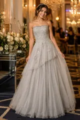 Vestido largo de fiesta color visón, con escote palabra de honor, corsé armado de encaje bordado con apliques florales y falda amplia de tul con volados irregulares.