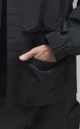 Chaqueta técnica liviana de microfibra con acabado mate, diseño con mangas desmontables que permiten convertirla en chaleco. Cuenta con cuello tipo camisa, cierre frontal oculto, cuatro bolsillos frontales de gran tamaño y puños elásticos. Incluye logo bordado en relieve en el pecho.
