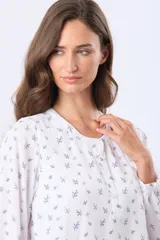 Blusa de manga larga con cuello redondo y cierre frontal de botones. Presenta un estampado floral en color negro sobre fondo blanco.