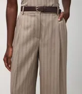 Pantalón de sastrería color beige con rayas verticales finas, de corte wide leg. Incluye un cinturón de cuero sintético marrón con hebilla metálica.
