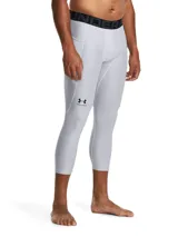 Calza deportiva de compresión tipo 3/4, color gris claro, con cintura elástica ancha negra con logo de la marca. Presenta paneles de malla para ventilación, bolsillo lateral y logo de Under Armour en la pierna.
