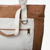Bolso tote de color marrón con bolsillo frontal blanco y asas de hombro en tono crudo.