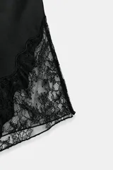Shorts satinados de tiro medio y cintura elástica, color negro, con detalles de aplicación de encaje a tono en los laterales y cierre frontal de botones.