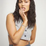 Pulsera de eslabones tipo bola de metal bañada en plata, con un dije central con forma de corazón irregular y un cierre de placa rectangular. Incluye un pequeño dije con la inscripción "UNO & 50".