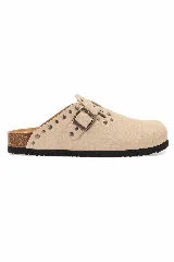 Zueco de ante color beige con tachas metálicas decorativas, tira con hebilla ajustable en el empeine, plantilla de corcho y suela de goma negra.