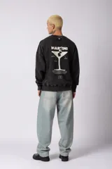 Buzo de cuello redondo con calce oversize y efecto lavado (washed). Presenta una estampa gráfica en la espalda con el diseño de una copa de martini y texto descriptivo.