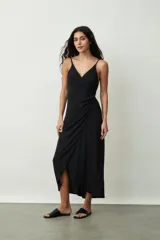 Vestido negro midi de tirantes finos, con escote cruzado en V y diseño envolvente con drapeado lateral que genera una abertura frontal.