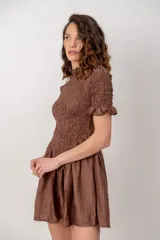 Vestido corto color marrón chocolate, con cuerpo fruncido tipo nido de abejas, cuello alto con volados y mangas cortas abuchonadas con terminación en volado. Presenta falda evasé con vuelo.