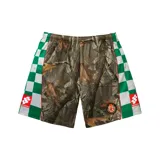 Short de fútbol Supreme con diseño de camuflaje tipo bosque en el panel central y franjas laterales con patrón de tablero de ajedrez en verde y blanco. Presenta parches con el logo de la marca y detalles en color rojo.