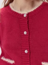 Cardigan de algodón grueso color rojo, con cuello redondo, cierre frontal de botones grandes y bolsillos cuadrados en el frente. Presenta detalles de pelo sintético en el cuello y los bolsillos, y logo bordado en uno de los bolsillos.