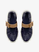 Zapato de cuero azul marino con correa marrón con hebilla dorada y suela de goma blanca con diseño ondulado.