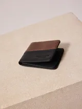 Billetera Rusty de cuero sintético bicolor, marrón y negro, con logo grabado.