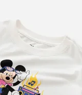 Remera crop de manga corta color blanco hueso, confeccionada en algodón con elastano. Presenta un estampado frontal de Minnie Mouse con gafas de sol, patines y un boombox, con la frase "La ratoncita quiere bailar".