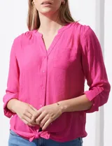 Blusa blanca de gasa marca Zac & Rachel, con cuello a la base, escote en V, abertura central con botones, bolsillo aplicado en el pecho y mangas largas regulables con presilla y botón. Tiene terminación opcional de nudo en el ruedo.
