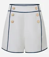 Short sastre de cintura alta confeccionado en crepé color blanco, con botones delanteros metalizados, cierre lateral por cremallera, bolsillos falsos atrás y bies contrastante en color negro.
