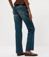 Pantalón de jean corte bootcut con tiro bajo, confeccionado en denim de algodón con lavado dirty que aporta un efecto envejecido. Presenta cierre frontal con botón y cremallera, presillas en la cintura y detalle de tachas metálicas en los bolsillos frontales.