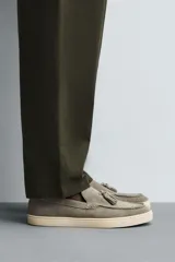 Mocasín casual de piel con acabado de serraje en color gris, con detalle de borlas en el empeine y suela plana a contraste en color beige.