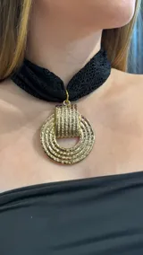 Gargantilla tipo choker de encaje negro con un dije circular grande de metal dorado con textura estriada.