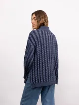 Sweater de punto con diseño de trenzas verticales, cuello alto y silueta oversize. Presenta un patrón bicolor en tonos azul y azul oscuro, con mangas largas y terminaciones en tejido acanalado.