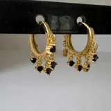 Par de aros tipo argolla dorados con dijes colgantes de circonitas negras.