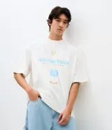 Remera de corte oversized color blanco, con cuello redondo y manga corta. Presenta una estampa frontal temática de Argentina en tonos celestes y dorados, que incluye el número 10, un sol y detalles gráficos tribales.