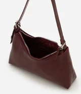 Cartera tipo baguette de tamaño pequeño en cuero sintético color bordó, con correa ajustable y cierre de cremallera metálica con herrajes en níquel.