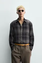 Camisa de corte relajado confeccionada en tejido fluido con mezcla de viscosa. Presenta diseño de cuadros en tonos grises y azul oscuro, cuello solapa, manga larga con puños abotonados y cierre frontal de botones.
