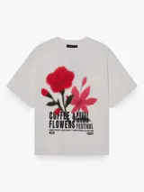 Remera de corte oversize y silueta boxy, color blanco, con cuello redondo y mangas cortas. Presenta una estampa frontal con diseño de flores en tonos rojos y rosados con efecto spray y tipografía negra.