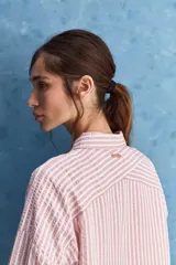 Camisa de calce relajado a rayas rosadas y blancas, con cuello camisero clásico y frente abotonado. Presenta recortes con cambio de dirección en las rayas y silueta amplia.