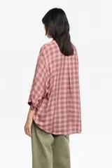 Camisa de manga 3/4 con cuello camisero, silueta ancha y bolsillo de plastrón en el pecho. Presenta un estampado de cuadros en tonos rosado y negro.
