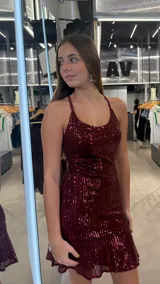 Vestido corto bordó cubierto de lentejuelas, con tirantes finos cruzados en la espalda, escote redondo y falda con volado en el ruedo.