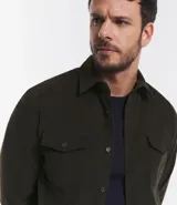 Camisa de hombre color verde oscuro, confeccionada en terciopelo, con cuello clásico, manga larga y dos bolsillos frontales con solapa y botón. Cierre frontal con botones.