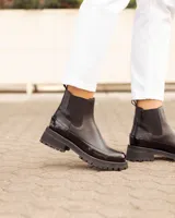 Botinetas tipo Chelsea de cuero negro, con paneles laterales elásticos y suela track dentada de goma. Presentan una combinación de texturas entre cuero mate y cuero charolado en la puntera y el talón.