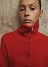 Jersey de punto grueso color rojo, de corte recto, con cuello polo amplio y cierre frontal de cremallera. Cuenta con mangas largas.