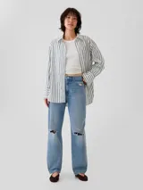 Camisa de corte oversize con estampado de rayas verticales finas en tonos rosados sobre fondo claro. Presenta cuello clásico, cierre frontal con botones, bolsillo en el pecho y puños anchos con botones.