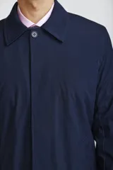 Gabardina de corte recto y estilo minimalista, color azul marino, con cuello camisero, cierre frontal oculto por solapa y puños ajustables con botón.