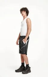 Bermuda negra de textil liviano con calce oversize, cintura elástica con cordón de ajuste y recortes decorativos en blanco. Presenta detalles reflectantes en los bolsillos delanteros y ribetes curvos blancos en la parte inferior.