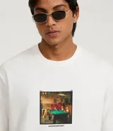 Remera de algodón color blanco, corte boxy, manga corta y cuello redondo. Presenta una estampa fotográfica localizada en el pecho de varios perros jugando al billar sobre una mesa verde.