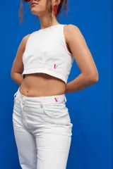 Pantalón de corte recto y tiro medio/alto, confeccionado en gabardina de algodón. Presenta bolsillos delanteros y traseros estilo jean, con costuras de pespunte en color rojo que contrastan con el tejido blanco.