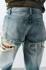 Jeans de tiro bajo y corte recto, color celeste con efecto lavado. Presenta diseño de doble tiro con detalle de short superpuesto con roturas, además de roturas adicionales en las perneras. Cuenta con cinco bolsillos, trabillas para cinturón y cierre frontal con cremallera y botón metálico.