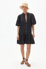 Vestido corto negro de lino con cuello mao, mangas cortas abullonadas, cierre frontal con botones y falda con volantes.