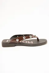 Sandalias tipo ojota de cuero marrón con acabado charol, con tiras decoradas con tachas metálicas esféricas y suela plana.