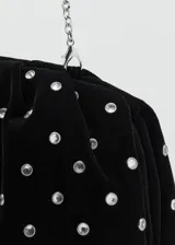 Bolso de mano negro de terciopelo, decorado con pedrería plateada distribuida en toda la superficie y cierre superior.