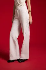 Pantalón jean blanco de corte flare y tiro alto, con detalles de tachas a lo largo de las costuras laterales y botamanga sin costura.