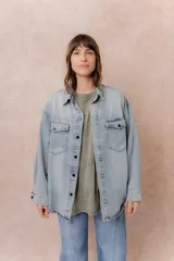 Camisa de jean de calce relajado y lavado claro con efecto vintage. Presenta cuello clásico, cierre frontal con broches metálicos, mangas largas con puños y dos bolsillos con tapa en el frente.