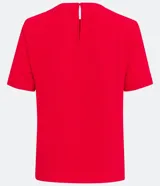 Blusa blanca de poliéster con cuello redondo, mangas cortas, cierre trasero en forma de gota, pequeñas aberturas laterales y acabados en pespuntes en las mangas y el cuello.