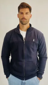 Campera de algodón color azul marino, con cierre frontal completo, cuello alto tipo bomber y bolsillos tipo canguro. Presenta un pequeño logo bordado en el pecho.