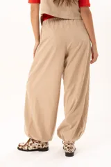 Pantalon tipo babucha de color beige, con silueta relajada y acabado suave tipo piel de durazno. Presenta cintura regulable con cordón y elástico en los tobillos que genera una forma abuchonada.